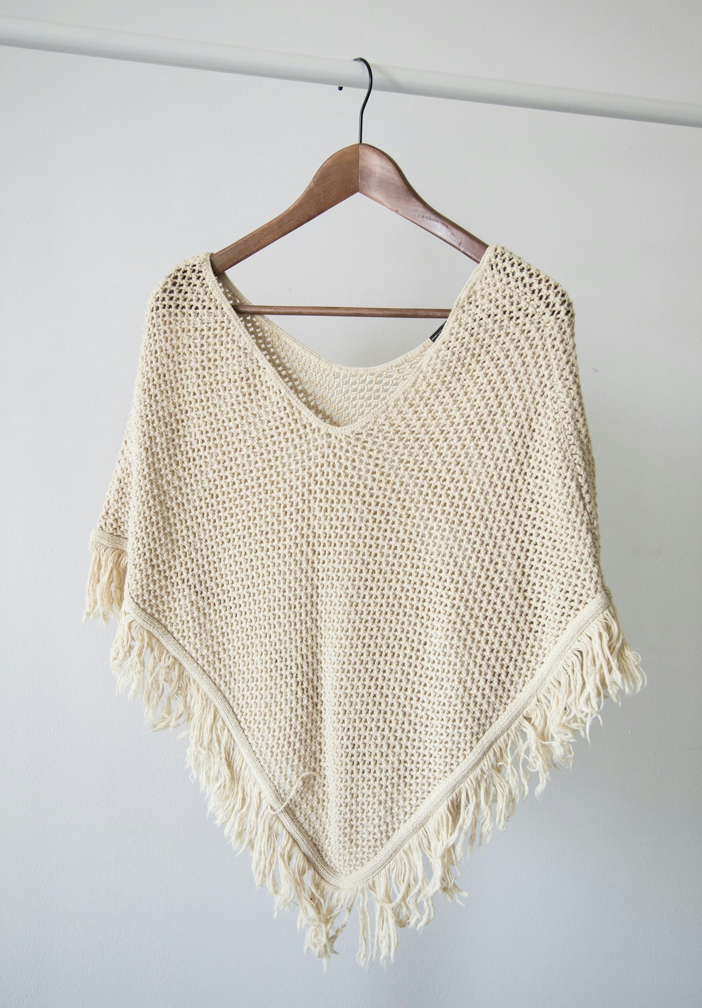 Cream open-knit wrap with fringe on a wooden hanger